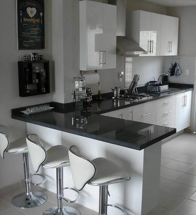 Cocina moderna con muebles de madera, encimera blanca, lámpara colgante negra y decoraciones de vidrio.