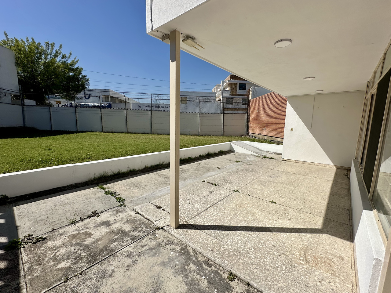 Sala de espera moderna y luminosa con sofás grises, plantas decorativas y grandes ventanales.