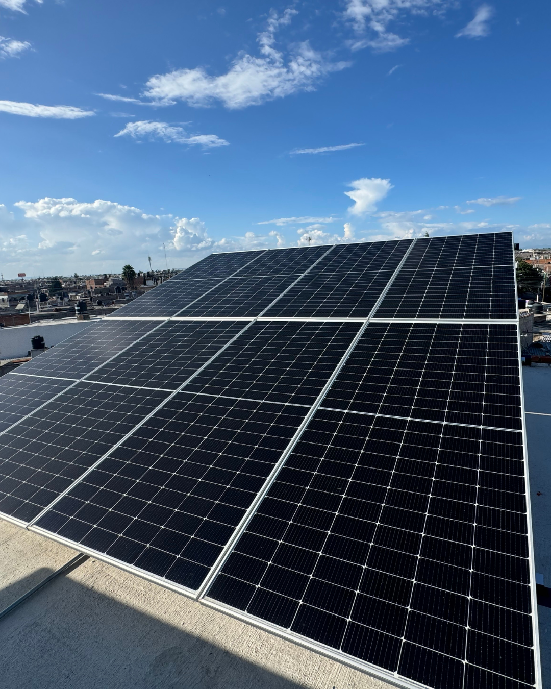Paneles solares en un campo verde con el sol brillando al fondo y cielo azul con nubes.