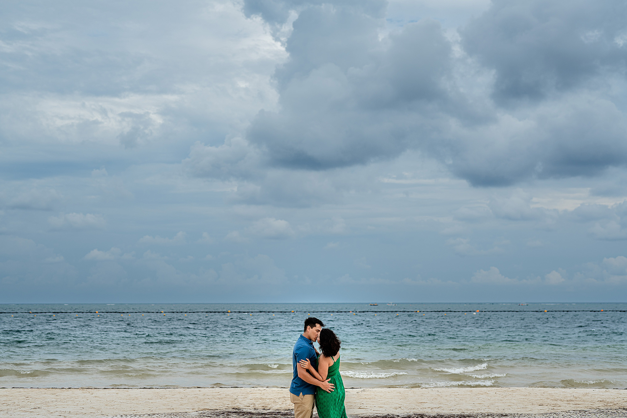 Pareja de novios abrazándose frente al mar Caribe durante pedida de mano en Puerto Morelos, Quintana Roo.