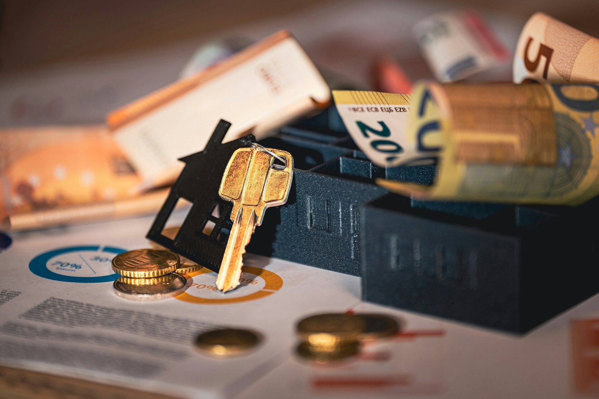 Llaves de casa, maqueta de vivienda y billetes de euro sobre documentos financieros e hipoteca