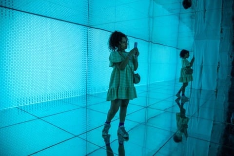 Mujer joven usando un smartphone en una sala iluminada en azul con paredes reflectantes.
