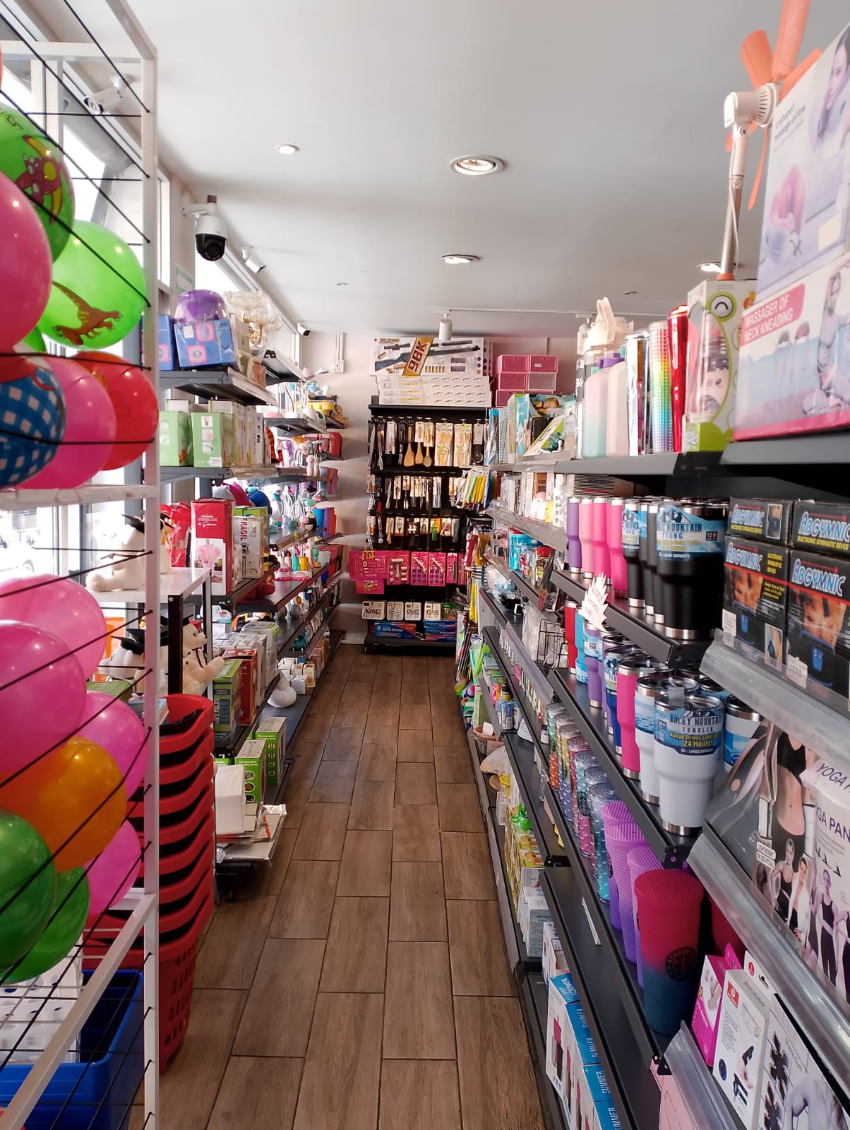 Pasillo de una tienda con estantes llenos de productos diversos, incluyendo pelotas de colores a la izquierda y artículos de cuidado personal a la derecha.
