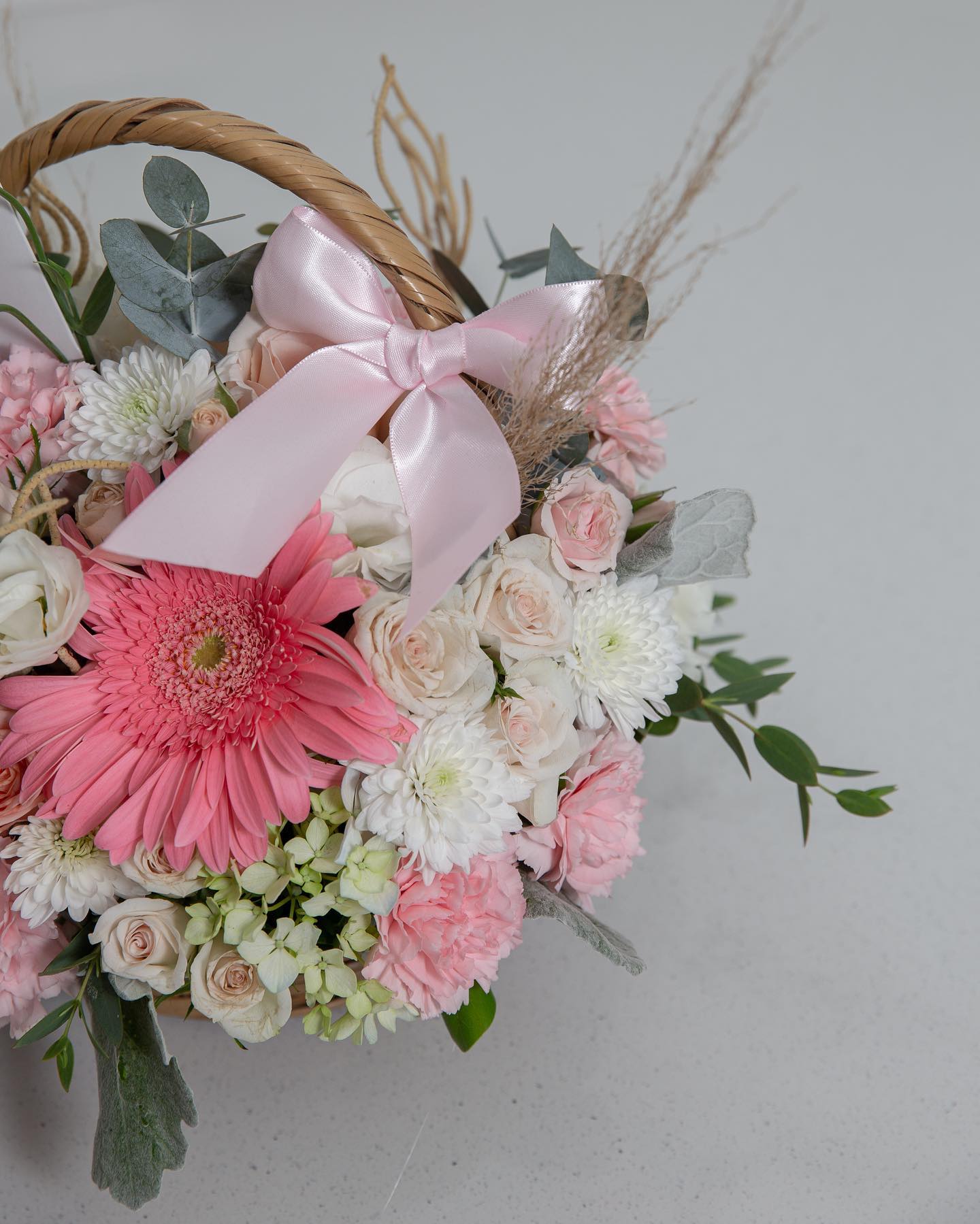 Arreglo floral de rosas y flores de color rosa y blanco en un jarrón de vidrio sobre una mesa de mármol, acompañado de libros y una jarra decorativa.