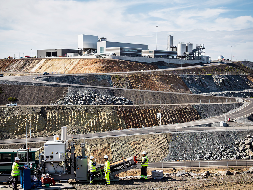 Planta industrial en mina a cielo abierto con carreteras, maquinaria pesada y trabajadores con chalecos de seguridad