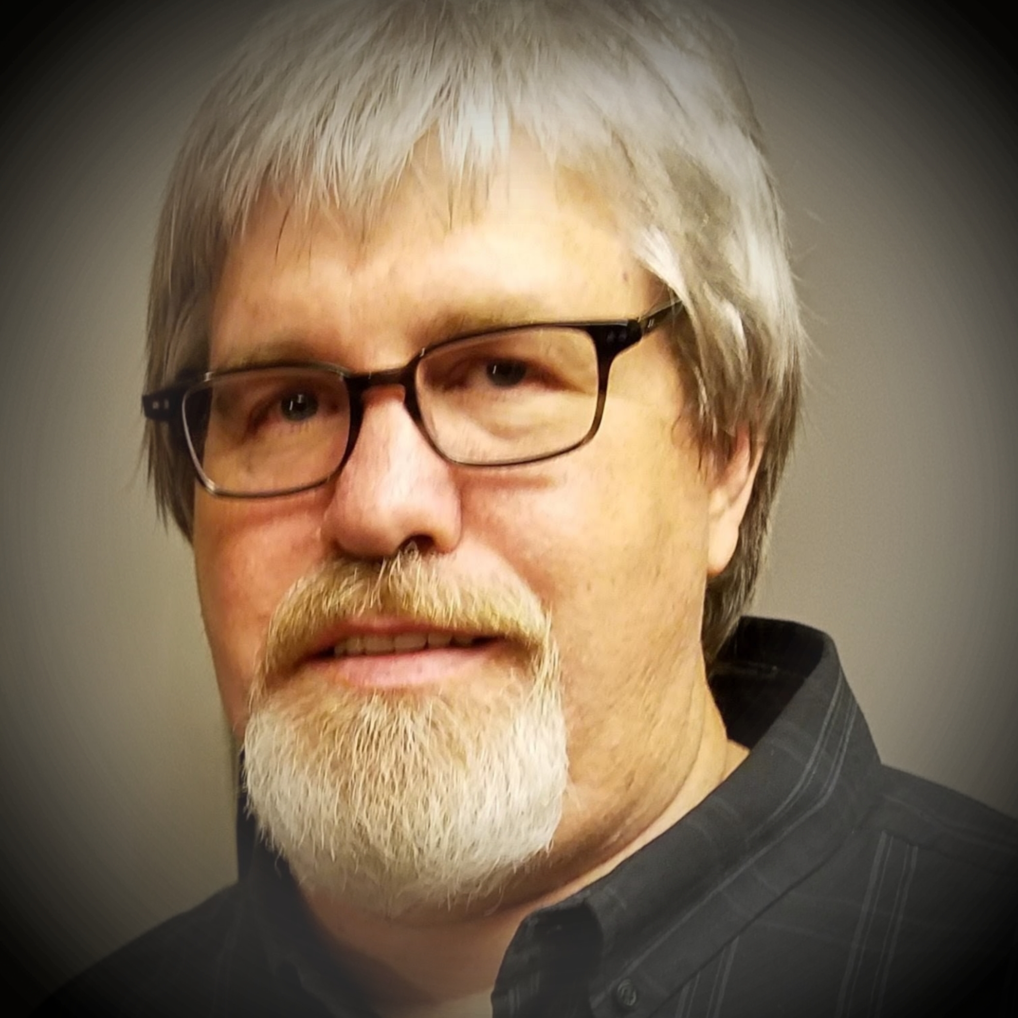 Portrait of a man with gray hair, glasses, and a beard wearing a dark shirt.