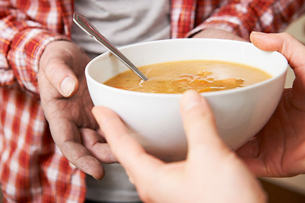 Homeless Man Being Handed Bowl Of Soup By Volunteer