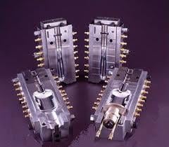 Four industrial metal molds with intricate designs, featuring multiple connectors, arranged on a dark background.