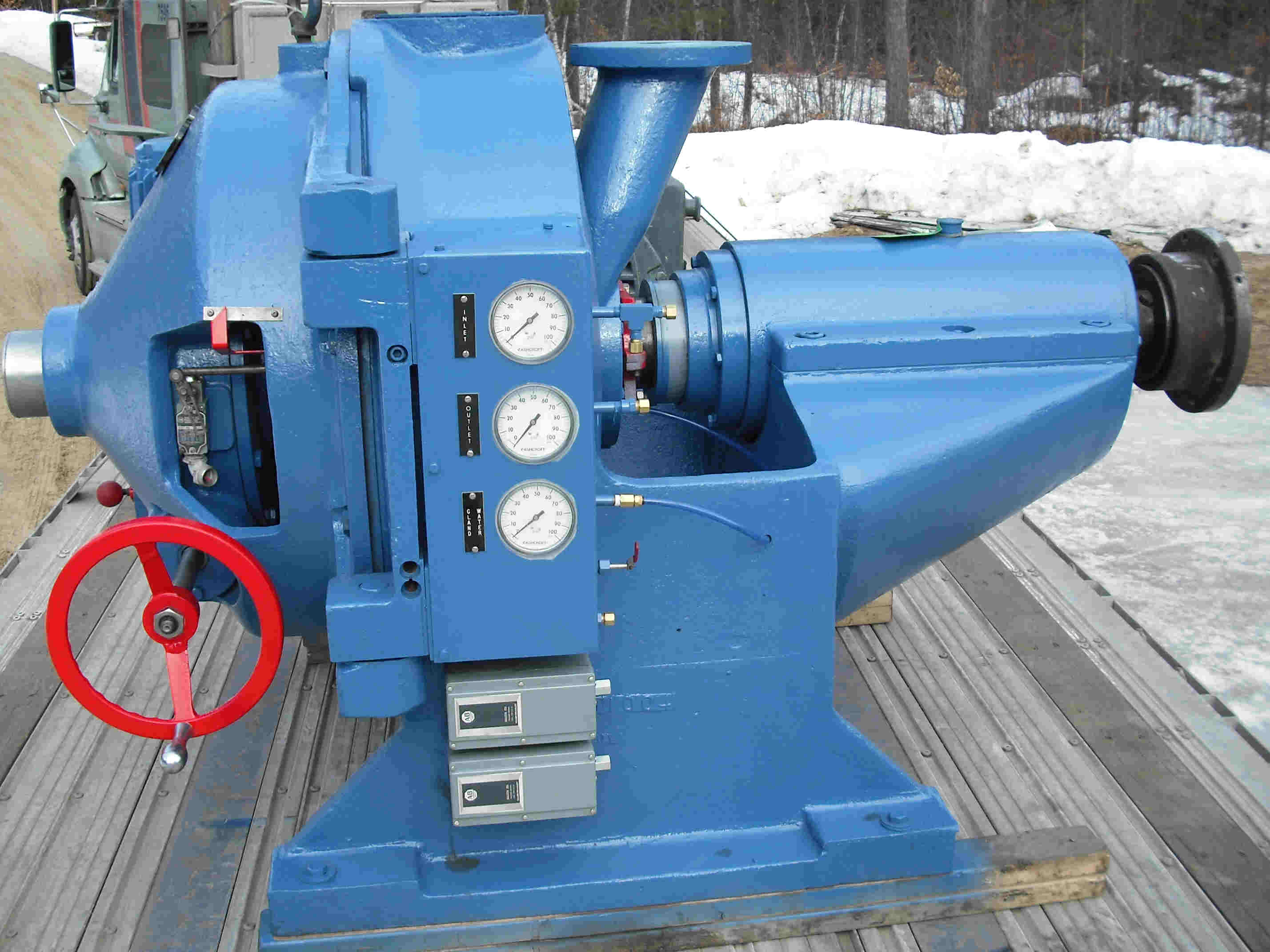 Modern industrial machinery in a factory setting with yellow and white equipment, control panel, and large coiled materials.