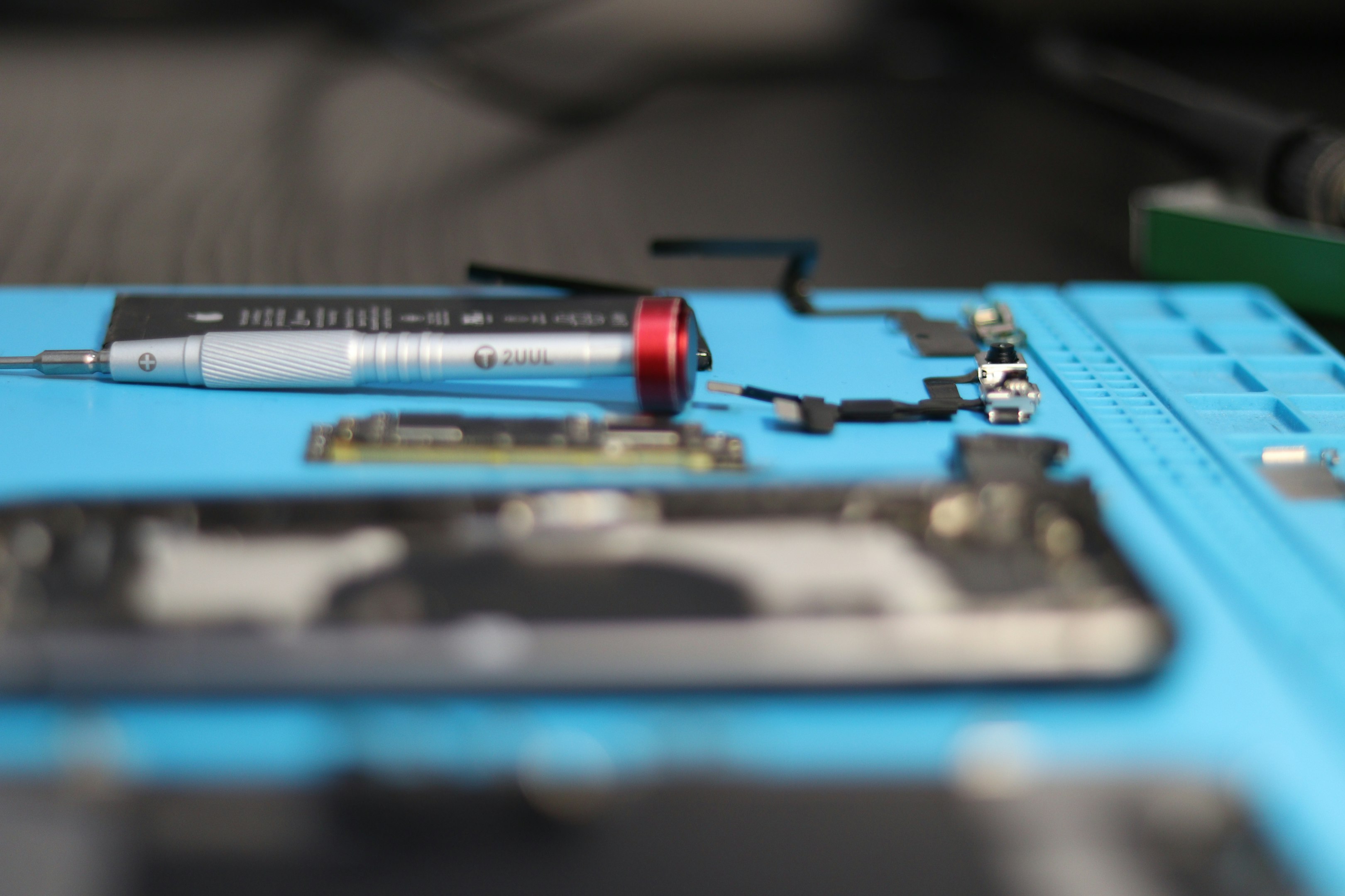 Primer plano de herramientas de reparación y piezas de teléfono móvil sobre una alfombrilla azul.
