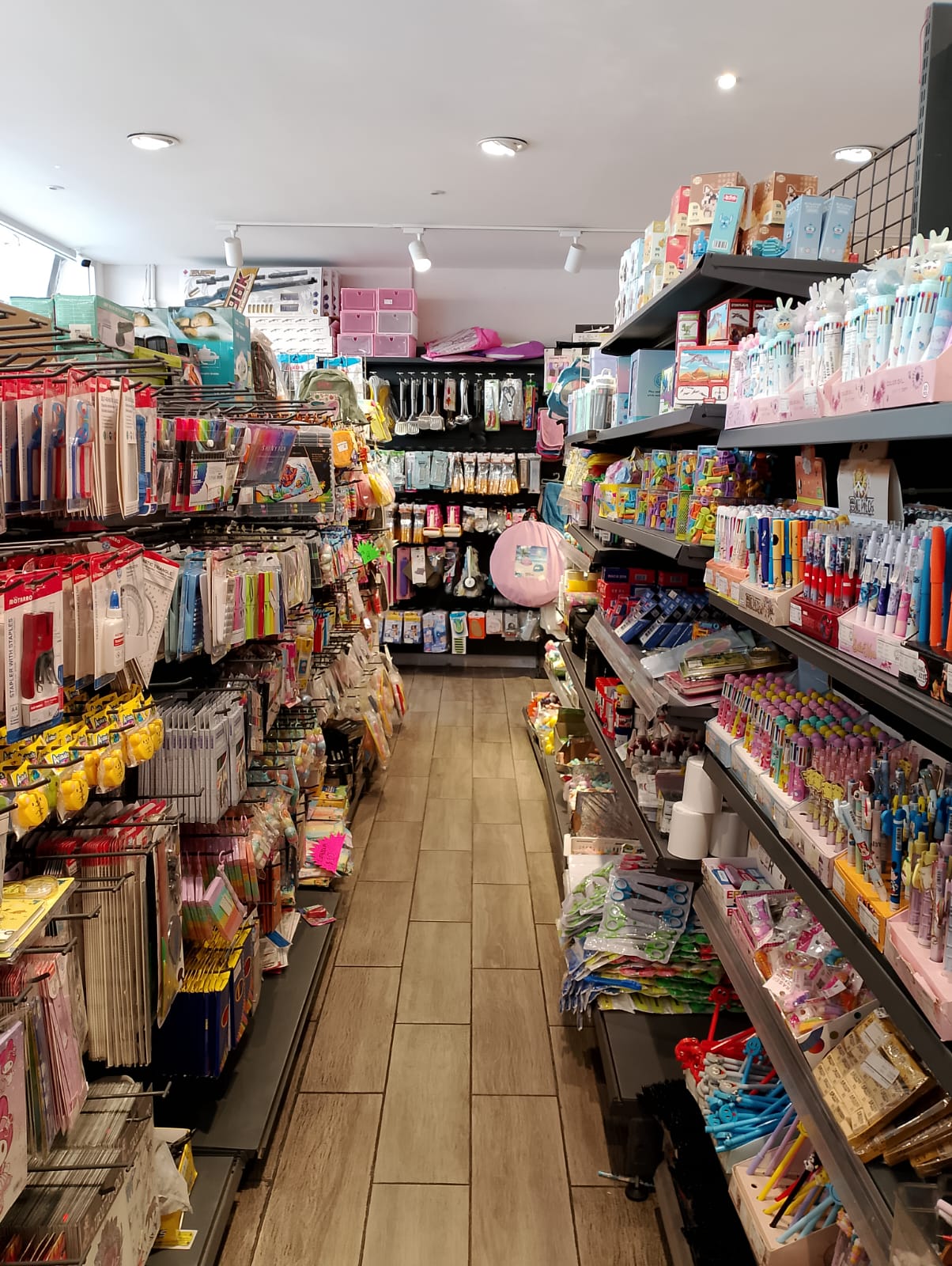 Pasillo de tienda de artículos de papelería con estantes llenos de productos escolares y de oficina.
