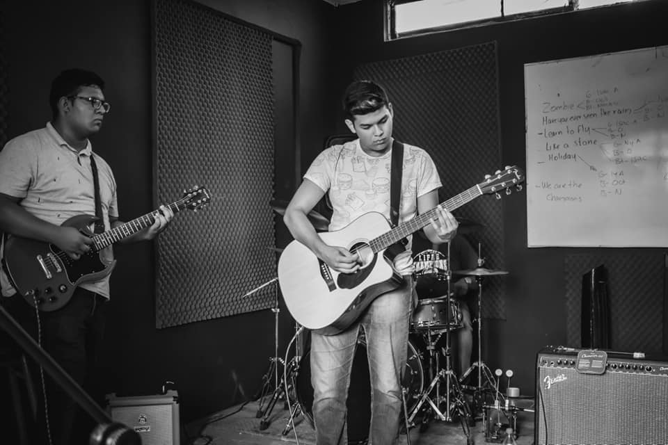 Banda de música ensayando en una sala insonorizada con dos guitarristas y un baterista.