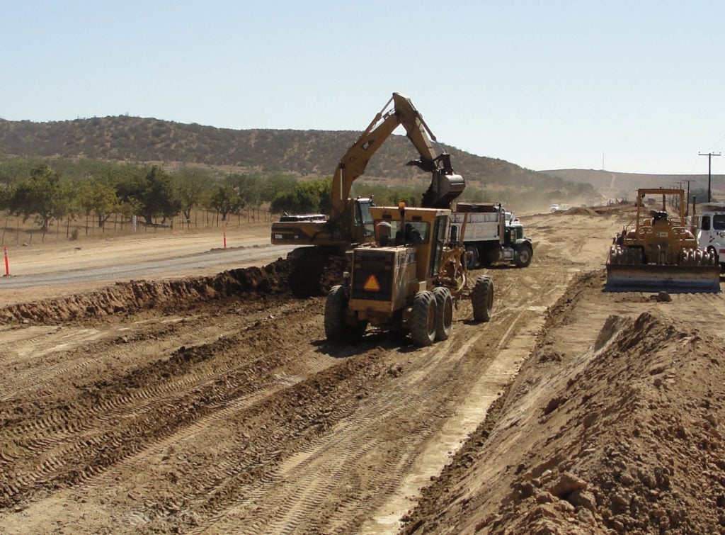 Maquinaria pesada trabajando en la construcción de una carretera en un entorno rural.