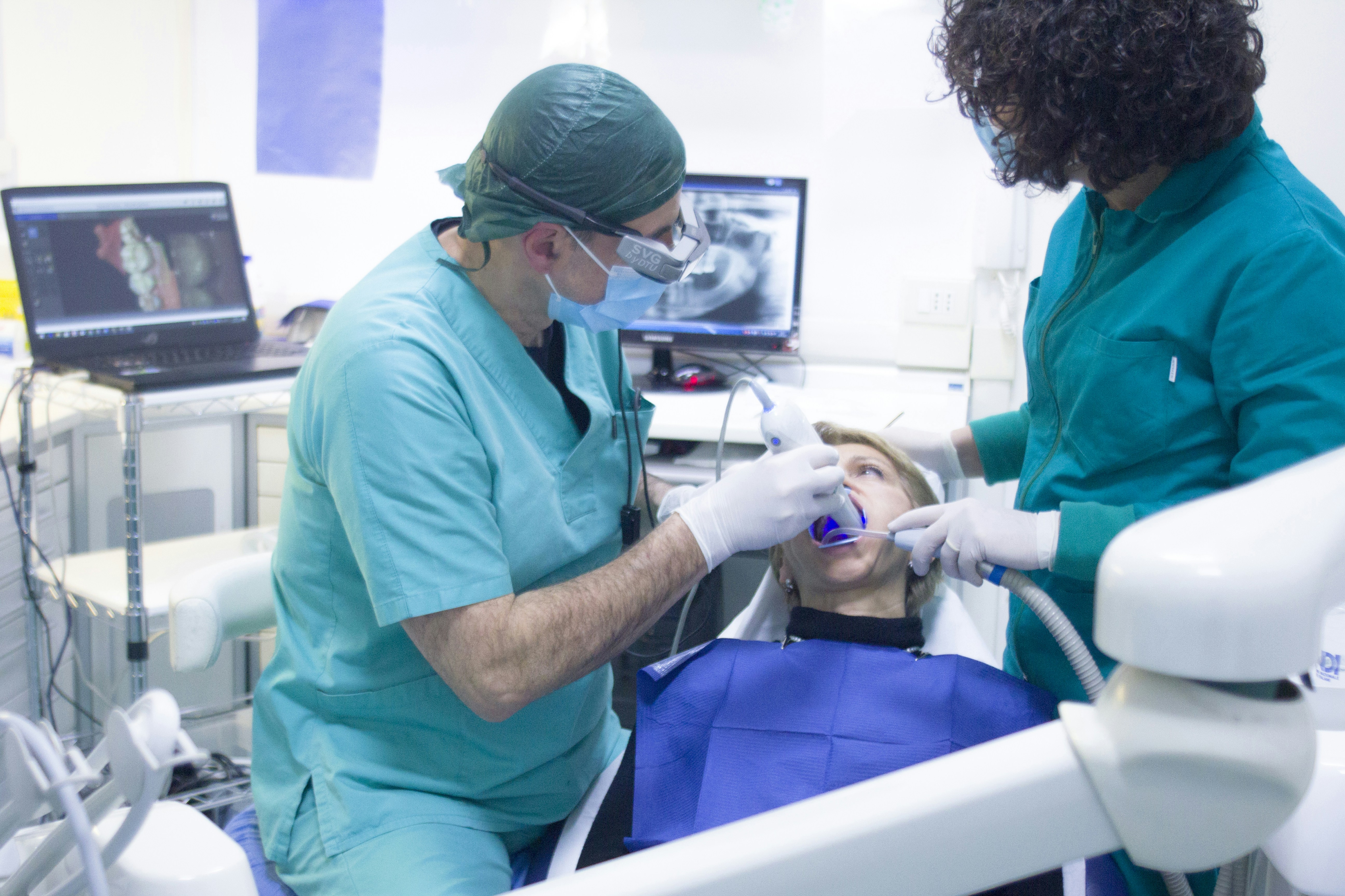 Dentist performing dental procedure using modern equipment on a patient in a clinic, with digital imaging displayed on monitors.