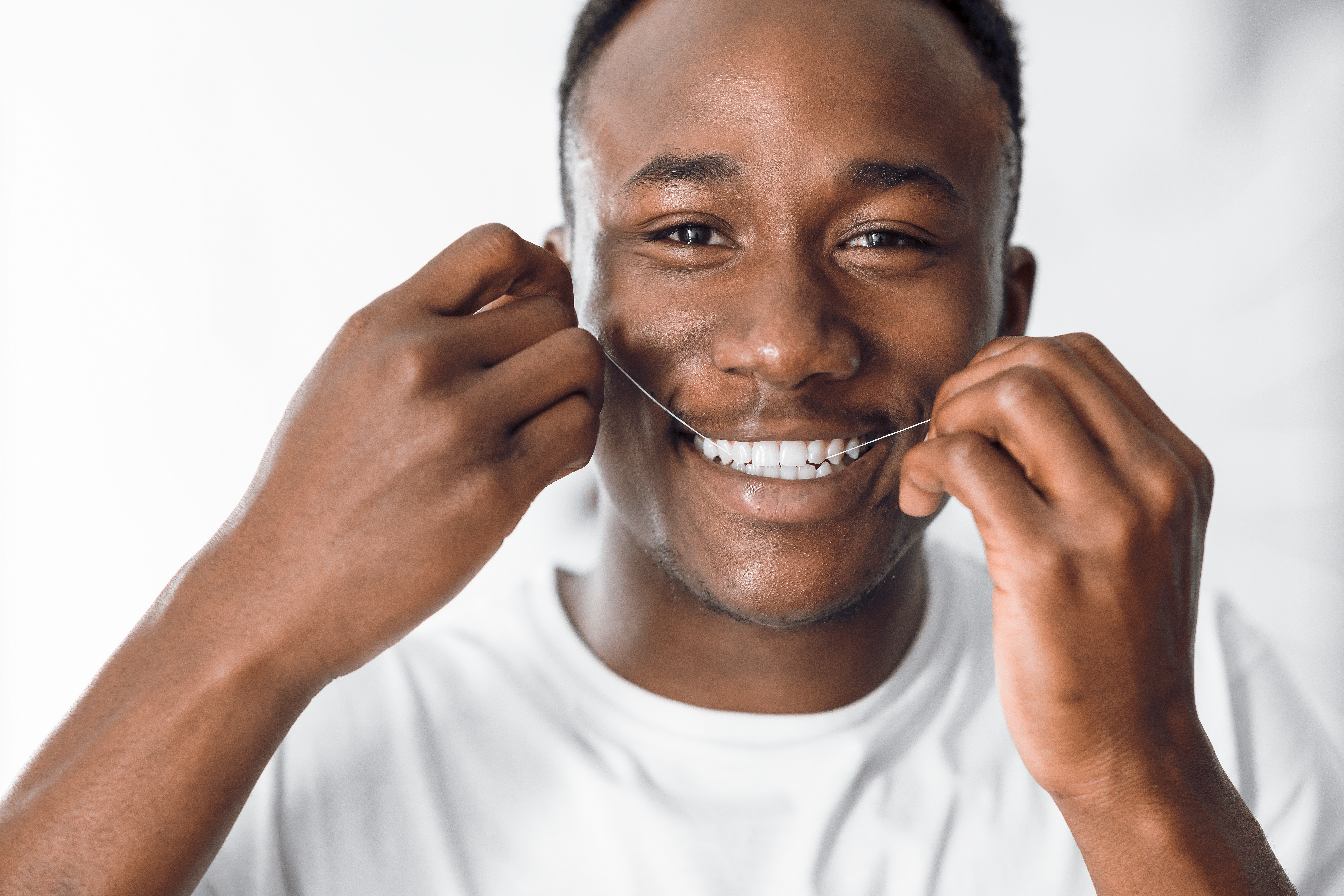 Black man smiles while flossing with a permanent retainer