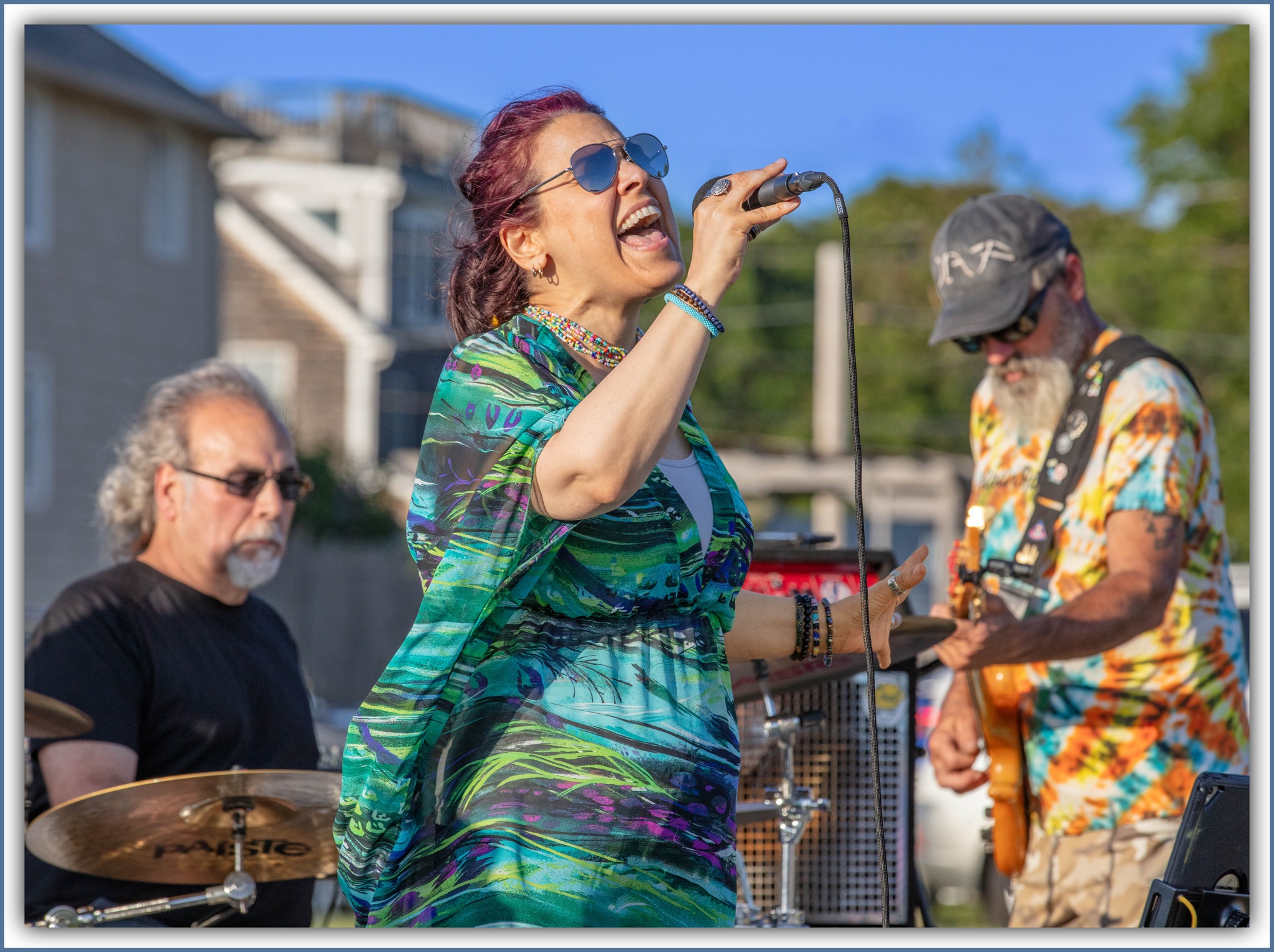 Musician performing at sunset with microphone, wearing cap and glasses, silhouette against the cloudy sky.