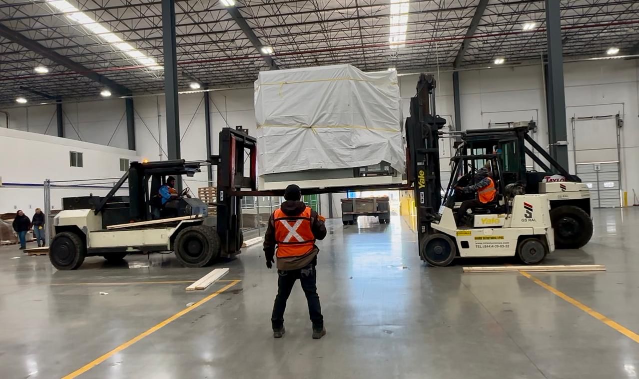 Trabajador con casco y chaleco de seguridad operando un carretilla elevadora amarilla en un almacén industrial.