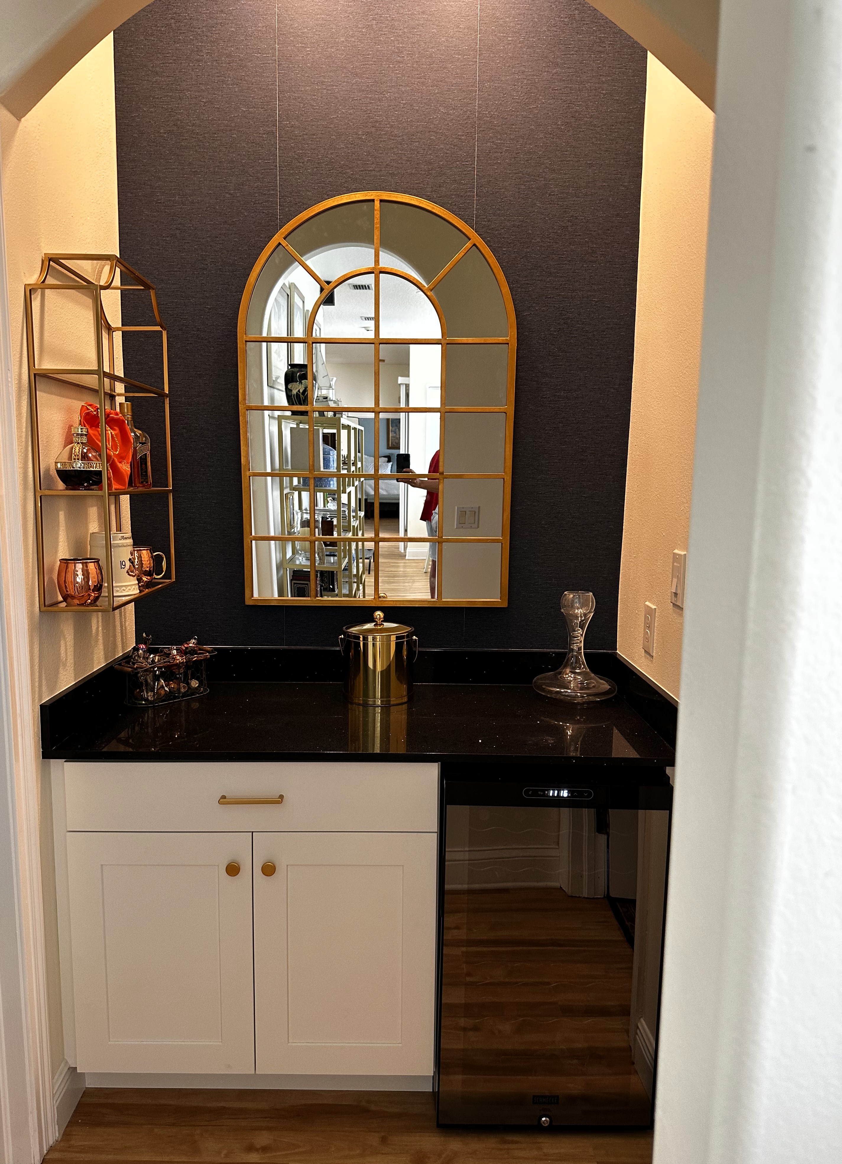 Inviting bar area showcasing arch, gold framed mirror, painted white cabinetry, and sleek Pompeii Black Magic quartz with matching 4" backsplash.