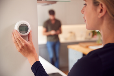 A woman adjusting a thermostat in her kitchen