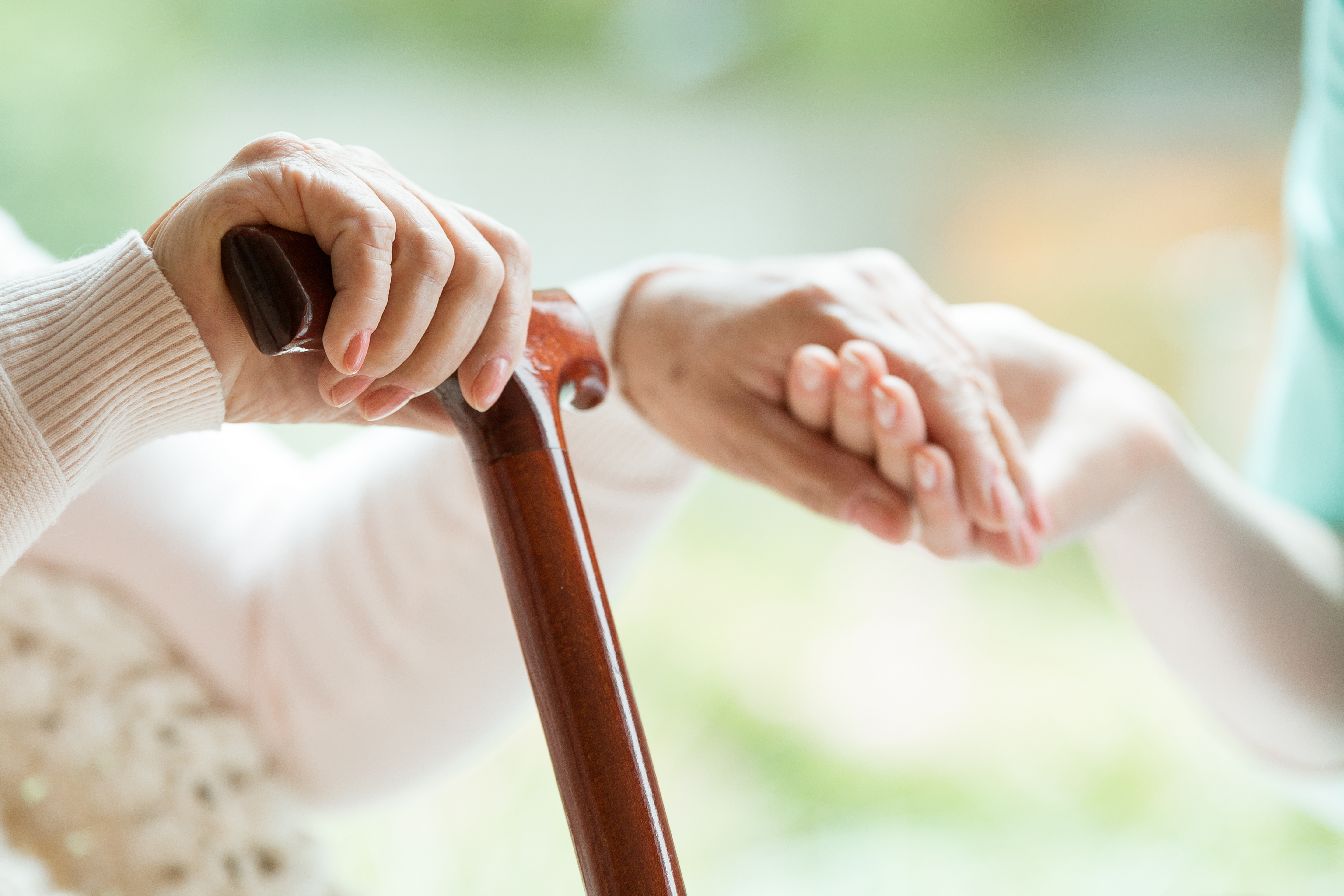 Elderly person's hand with cane being held by a caregiver, symbolizing support and care.