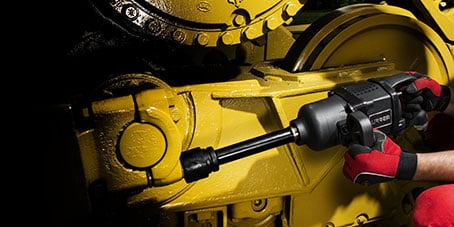 Herramienta eléctrica siendo utilizada para reparar maquinaria industrial amarilla.