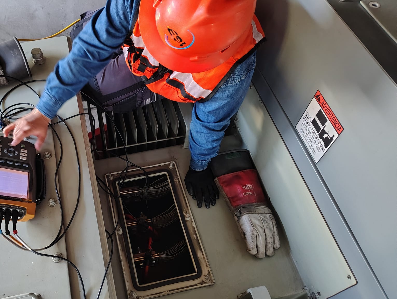 Ingeniero con casco y guantes de seguridad trabajando en un laboratorio con un monitor de computadora.