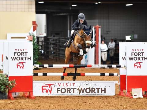 Equestrian rider jumping over an obstacle at Fort Worth event inside an arena.