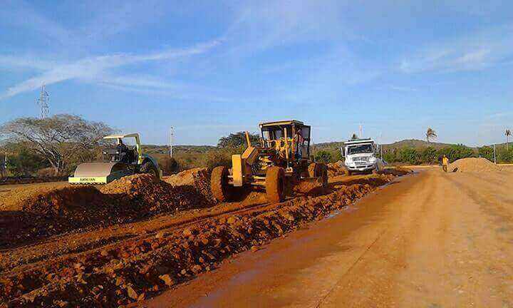 Maquinaria pesada nivelando tierra en una construcción de carretera bajo un cielo azul.