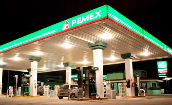Camión blanco detenido en una gasolinera moderna con surtidores anaranjados y cielo despejado.