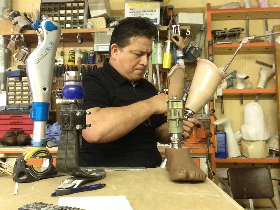 Prosthetist adjusting a prosthetic leg in a workshop with prosthetic limbs and orthotic tools