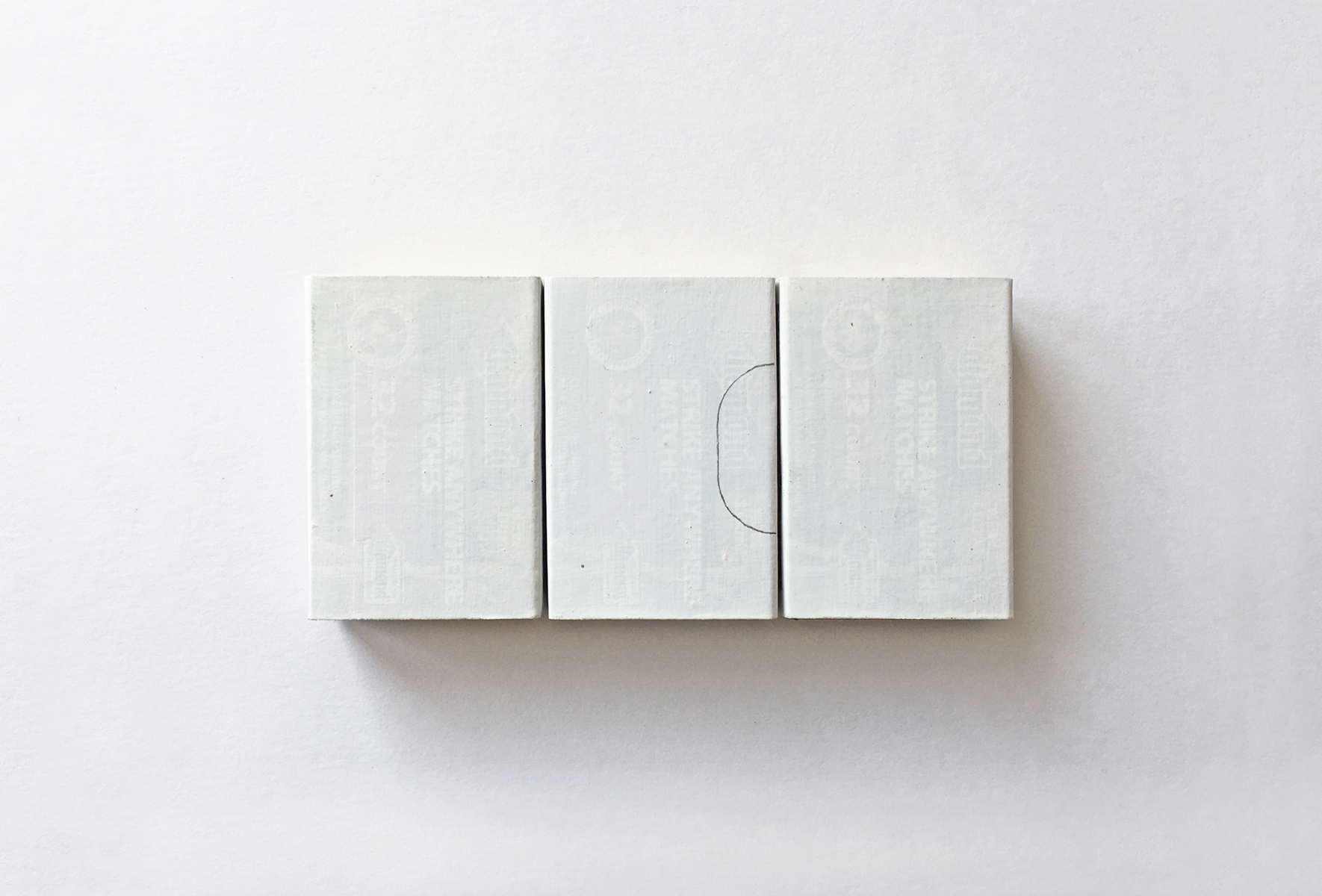 Three matchboxes painted white with a half oval shape pencil outline on one.