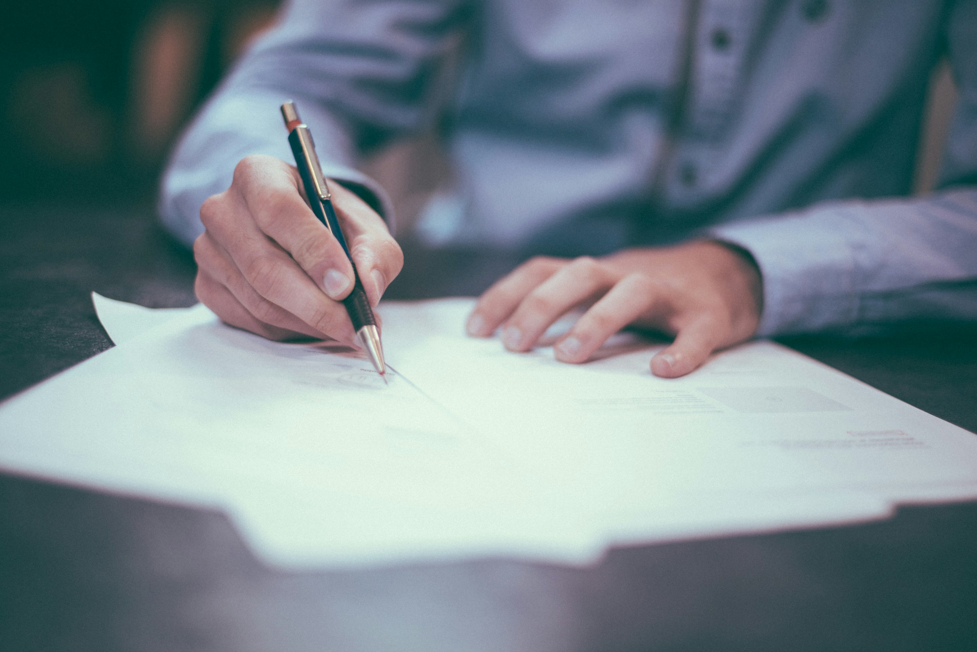 Close-up of a person signing a document with a black pen on paper