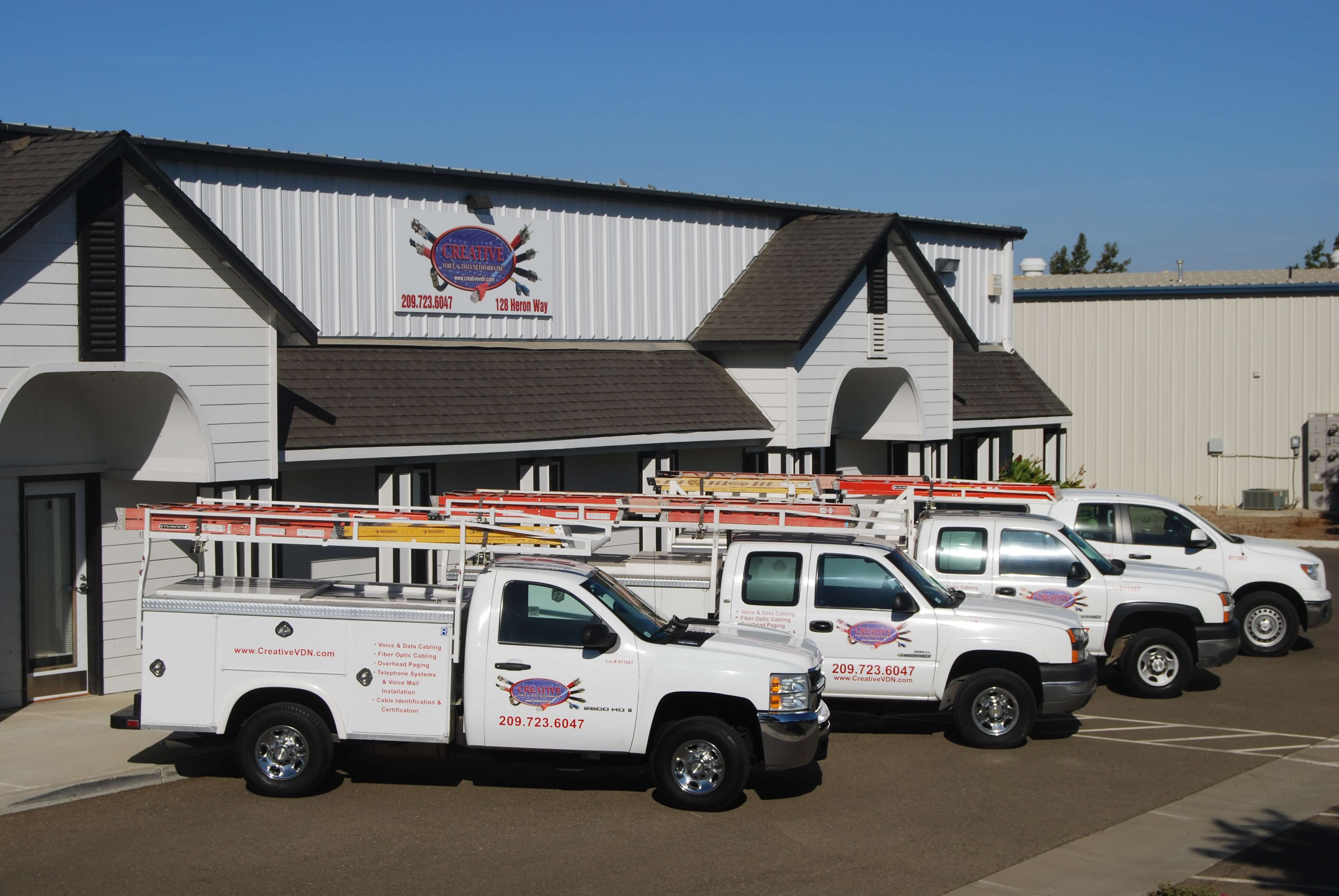 Fleet of service trucks with ladders parked in front of Creative building, featuring company logo and contact details.