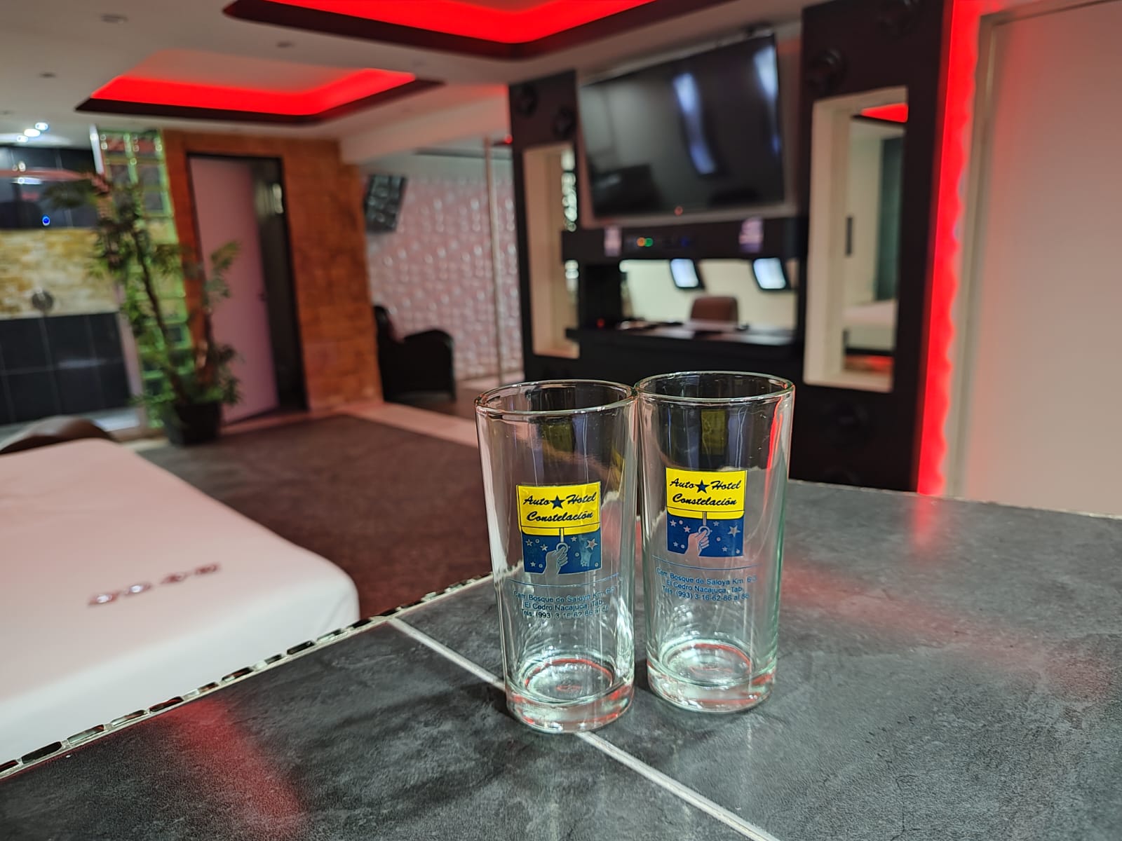 Habitación de hotel moderna con iluminación roja, vasos decorativos en primer plano y pantalla de televisión en la pared.