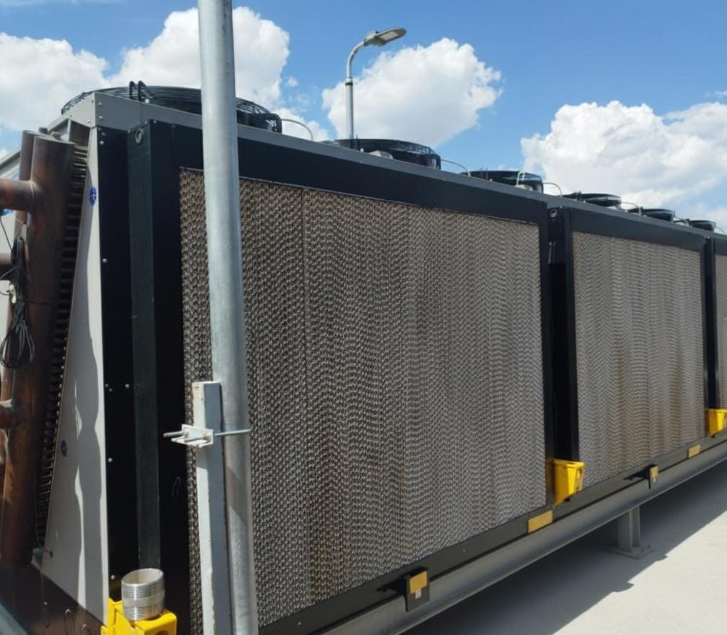 Unidad de refrigeración industrial en un tejado bajo un cielo azul con nubes esponjosas.