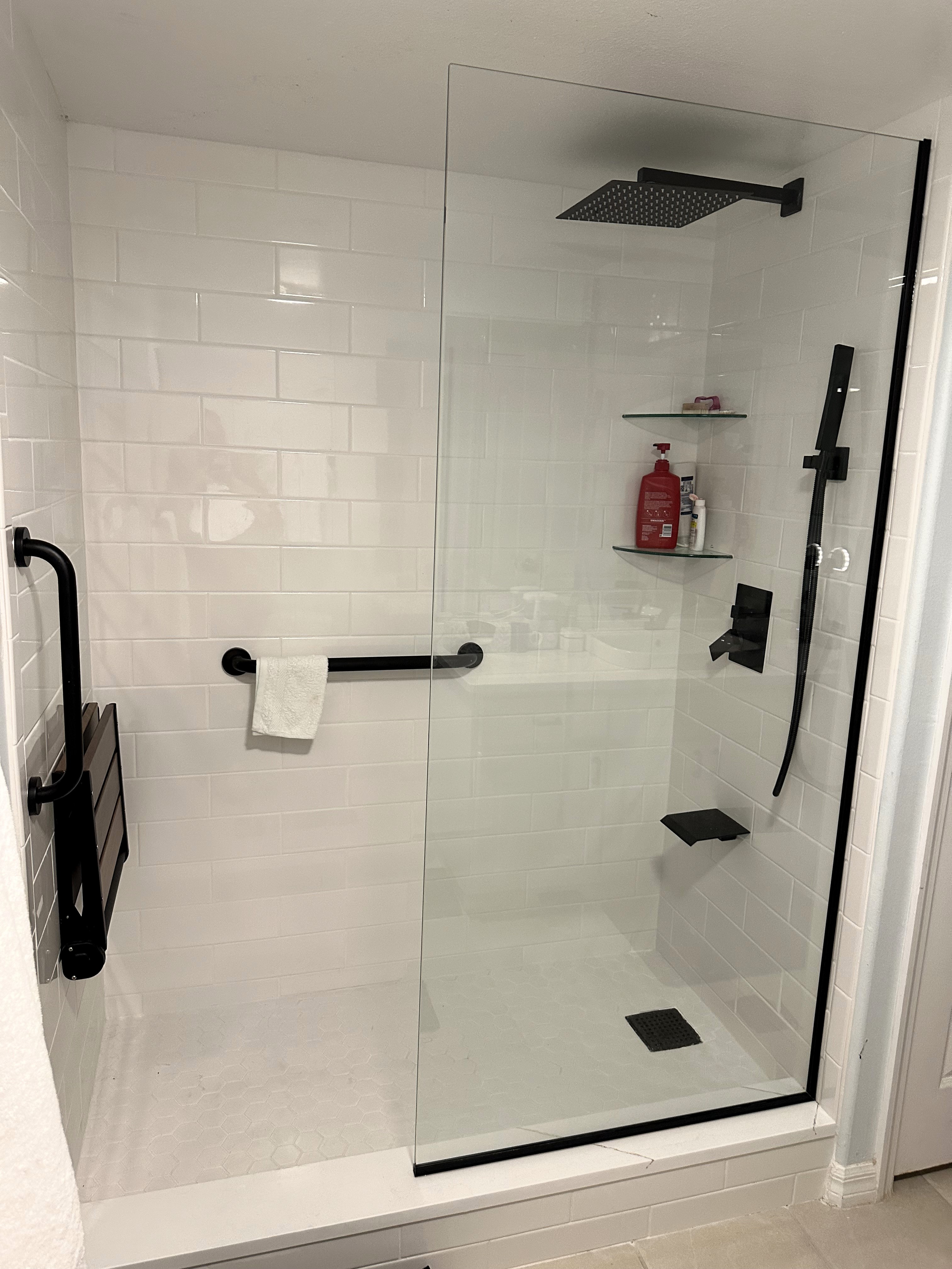Clean and bright walk-in shower featuring 4x12 glossy white wall tile and eye-catching matte black grab bars, bench, drain, and shower fixtures.