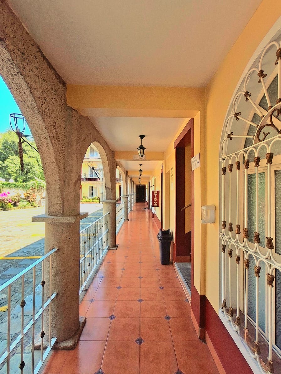 Calle empedrada con casas coloniales coloridas, balcones de hierro, autos estacionados y montañas al fondo