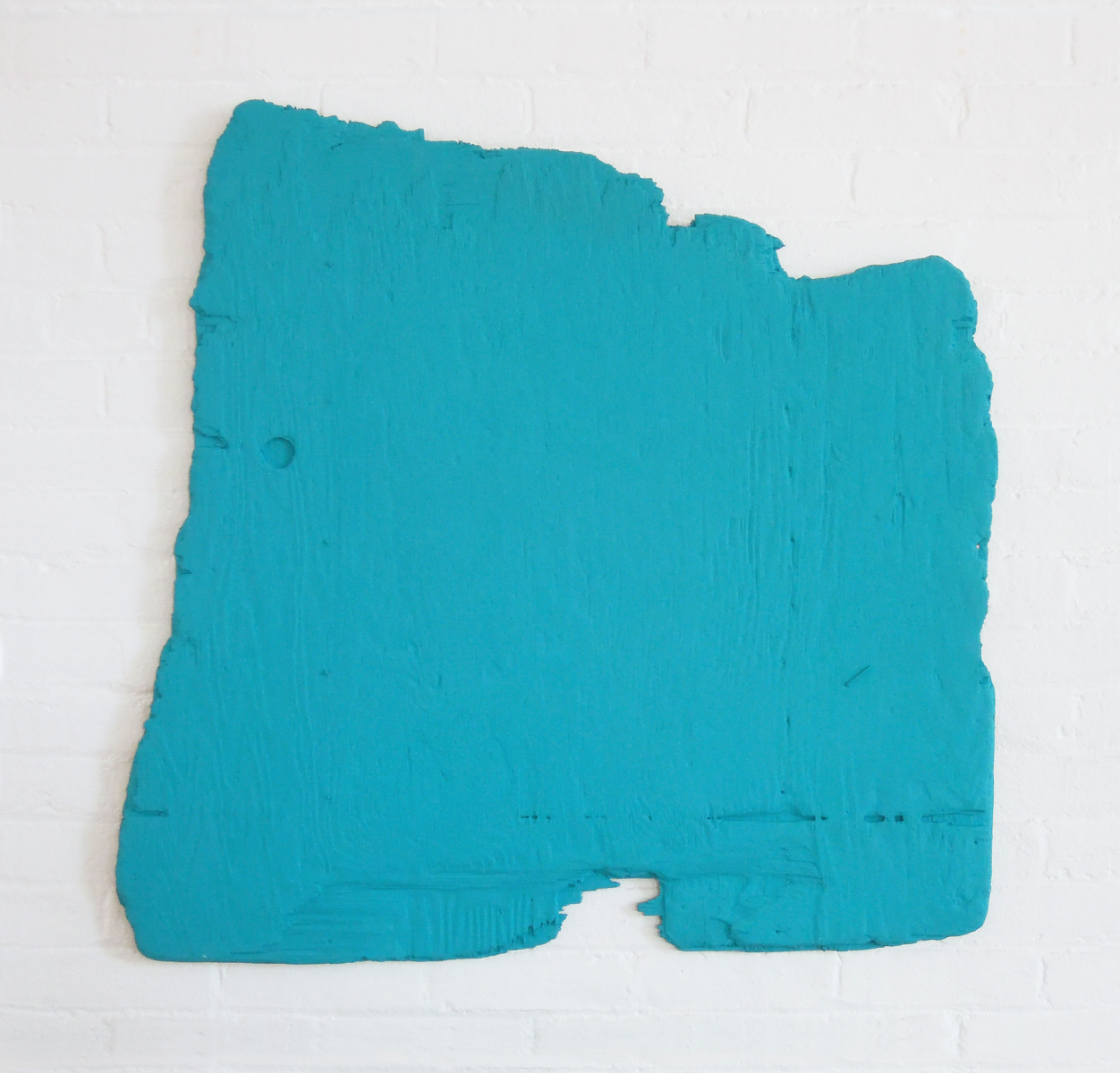 An irregularly shaped piece of plywood completely covered in turquoise paint.