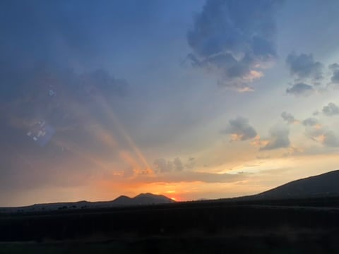 Puesta de sol con cielo nublado y rayos de luz sobre montañas en el horizonte.