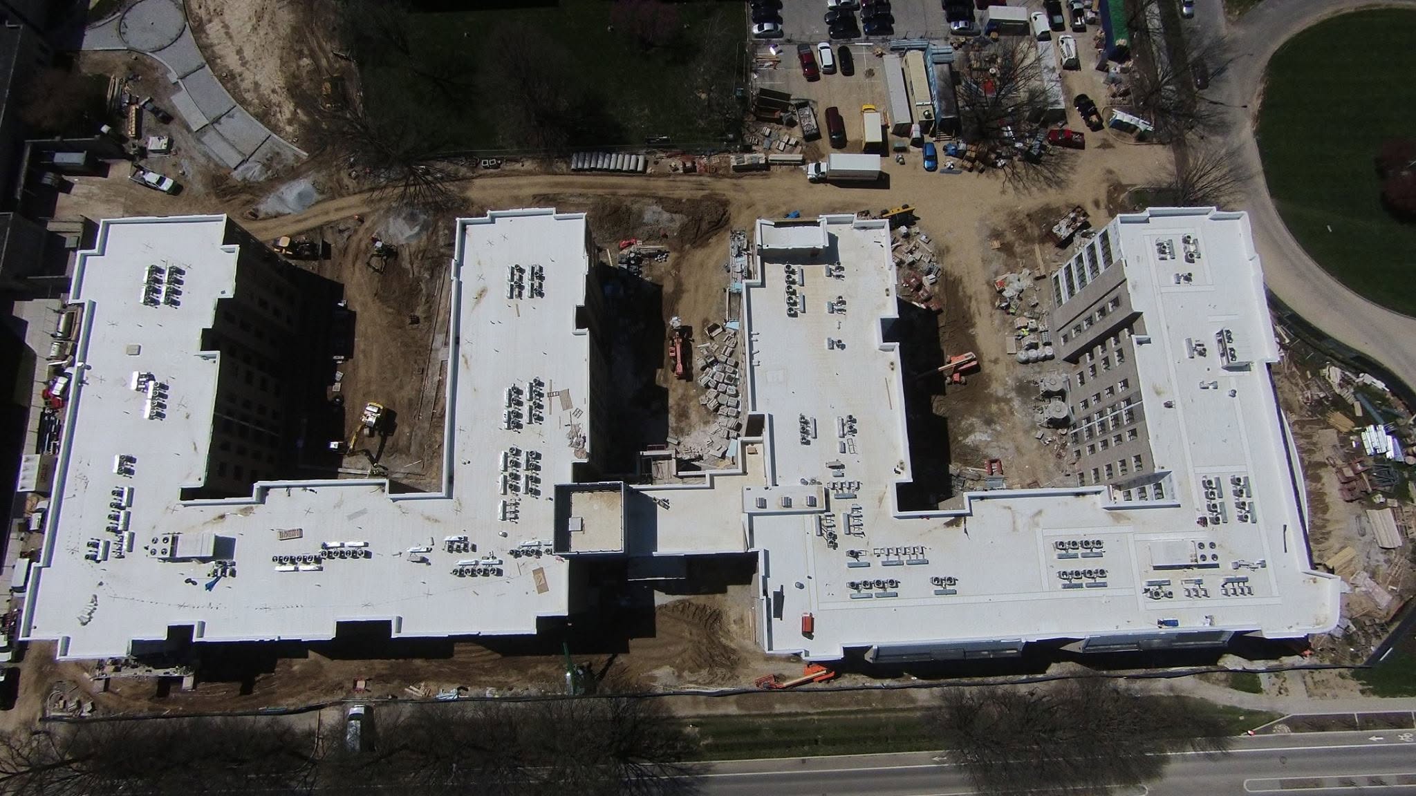 Aerial view of large commercial building construction site with white rooftops, equipment, vehicles, and dirt access roads