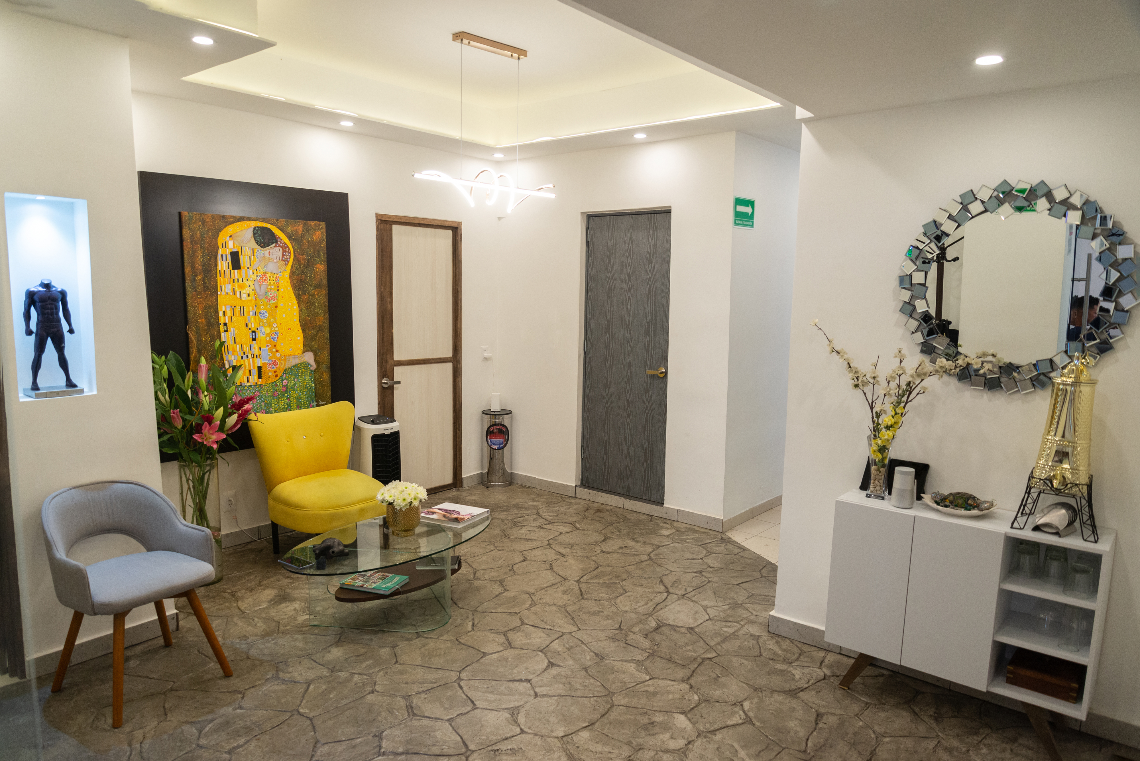 Sala de spa moderna con camilla, muebles blancos, plantas decorativas y luz natural.