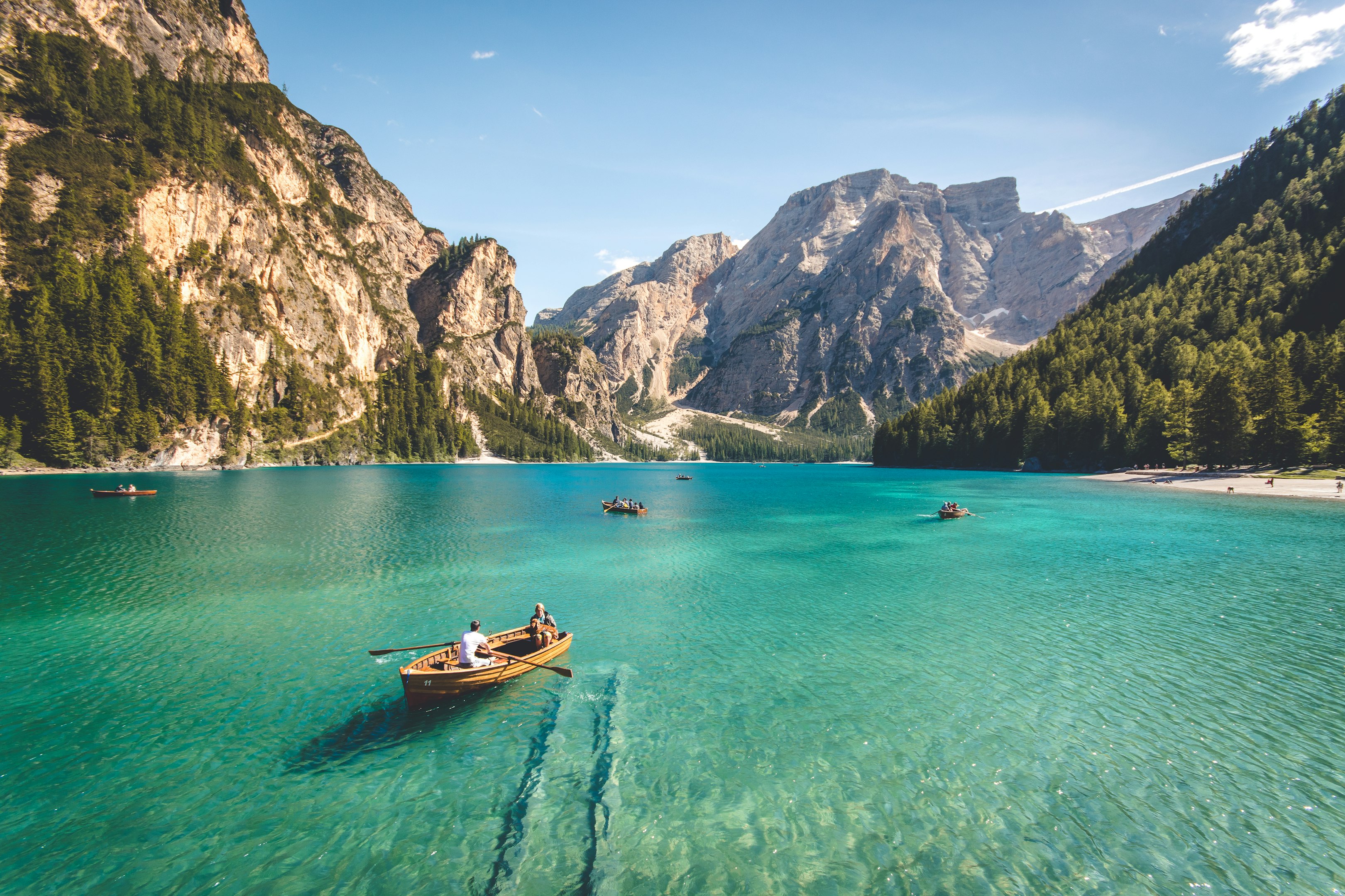 Scenic view of crystal-clear lake with wooden boats and pine-covered mountain backdrop under blue sky.