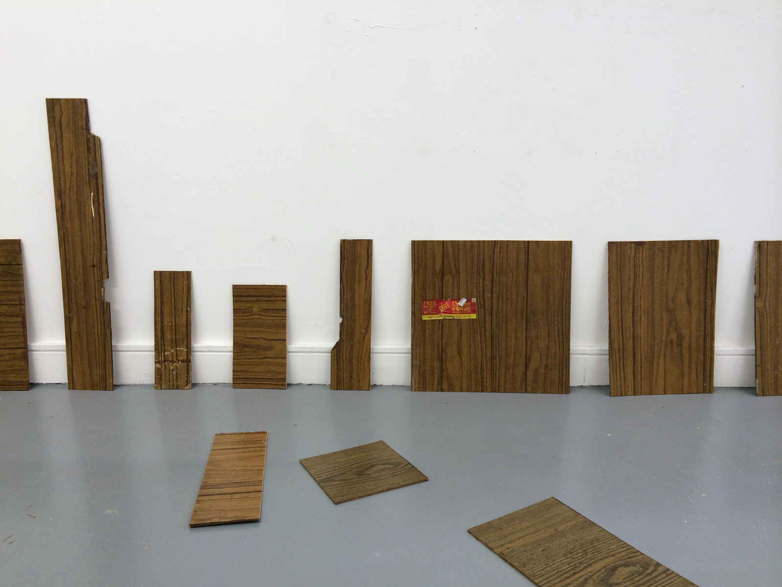 11 wood panel pieces of various shapes leaning against a wall and on the floor.