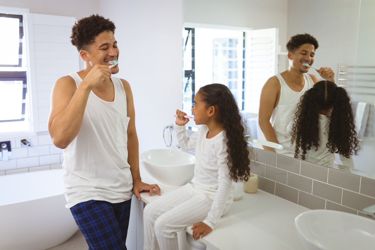 father and daughter brushing teeth together to prevent white plaque on teeth