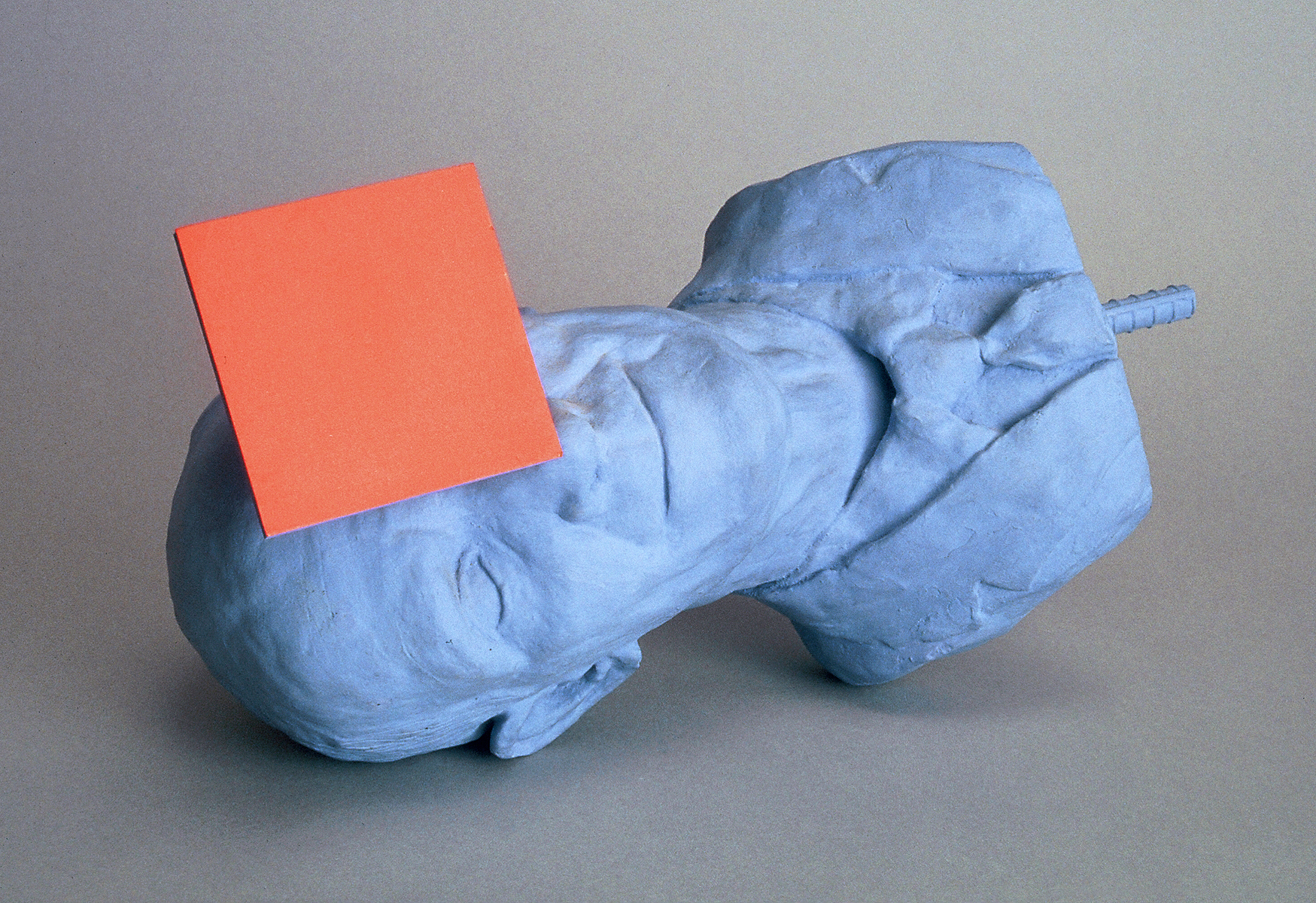 A blue painted statue head of a man in a jacket and tie, plus an orange square.