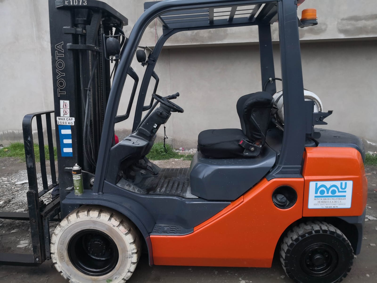 Cargador frontal amarillo con accesorios, estacionado en una superficie de cemento bajo un cielo parcialmente nublado.