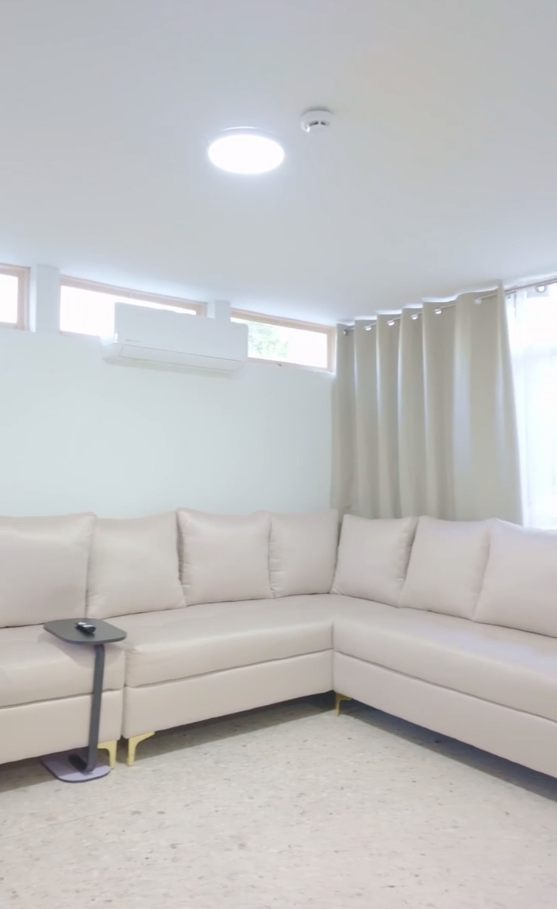 Sala de estar moderna con sofás beige, cojines de colores, muebles de madera, plantas decorativas y luz natural.