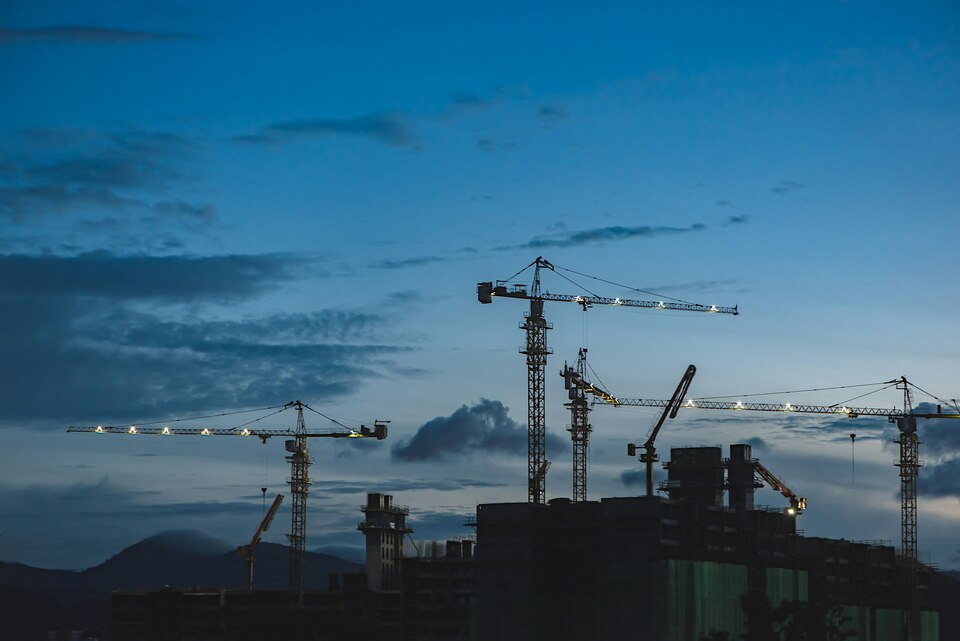 Grúas de construcción trabajando al anochecer con cielo azul y nubes. Grúas de construcción trabajando al anochecer con cielo azul y nubes.