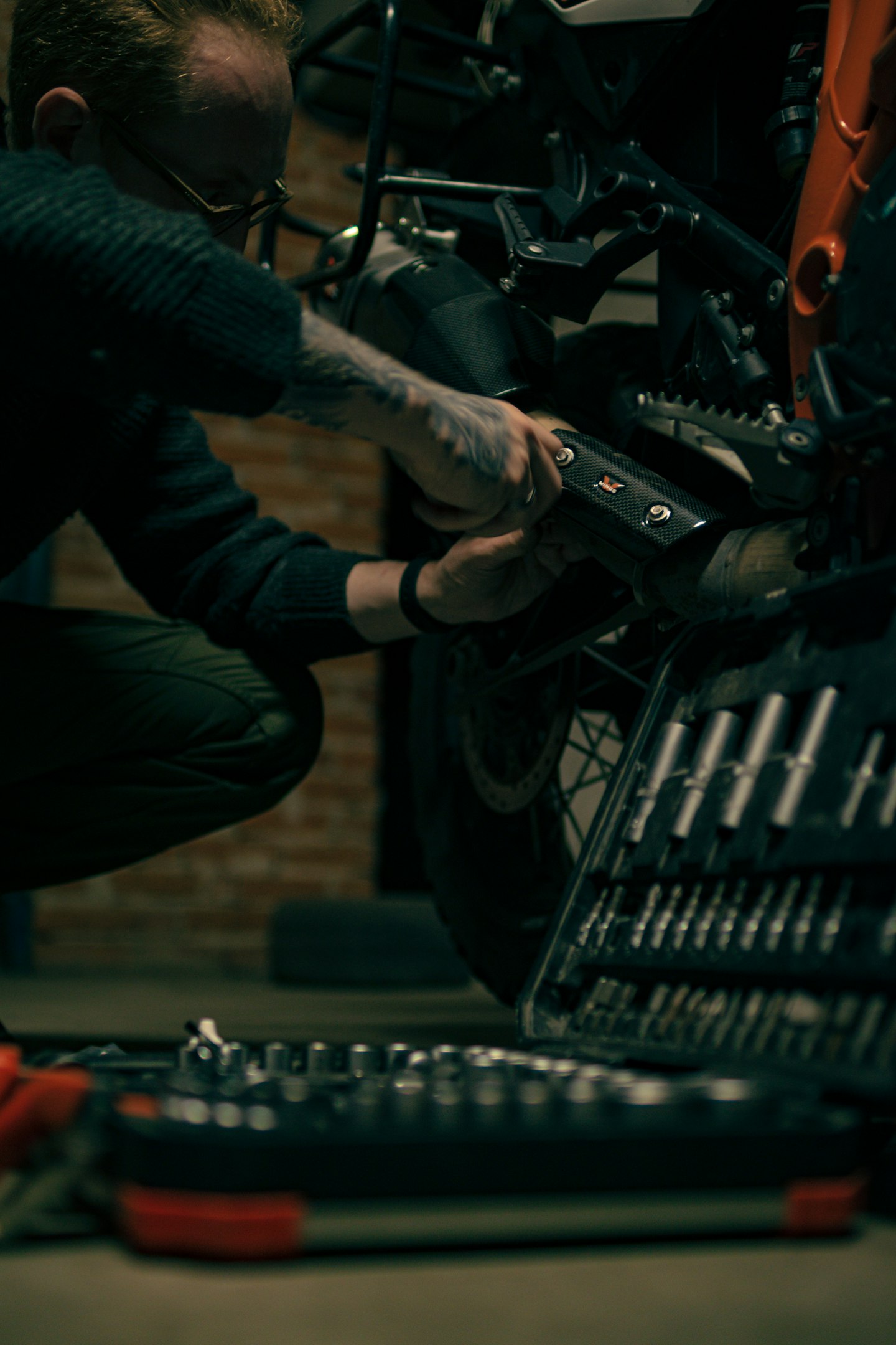 Person working on a motorcycle with tools in a dimly lit garage.