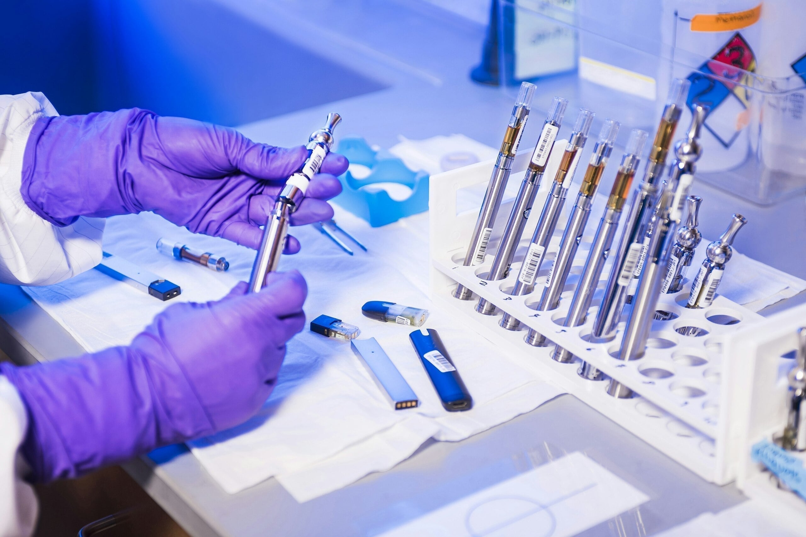 Técnico con guantes morados ensamblando cartuchos metálicos de vapeo en laboratorio